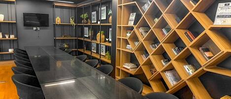 A conference room with a long black table, black chairs, and wooden bookshelves filled with books.