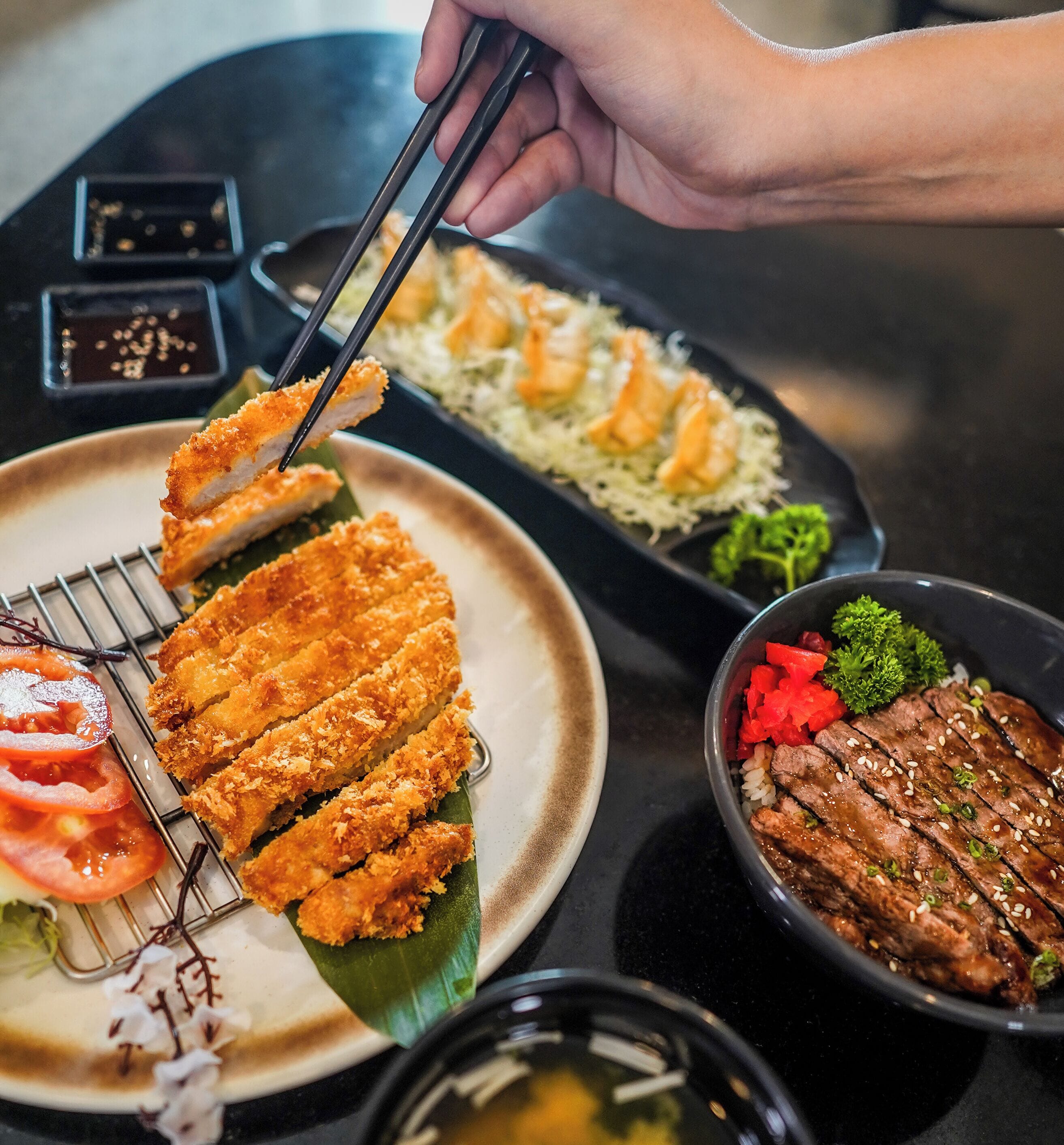A variety of Japanese dishes including tempura, rice, and grilled meat, served on a black table.
