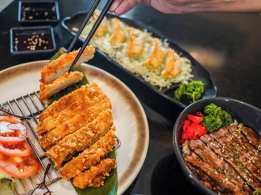 A variety of Japanese dishes including tempura, rice, and grilled meat, served on a black table.