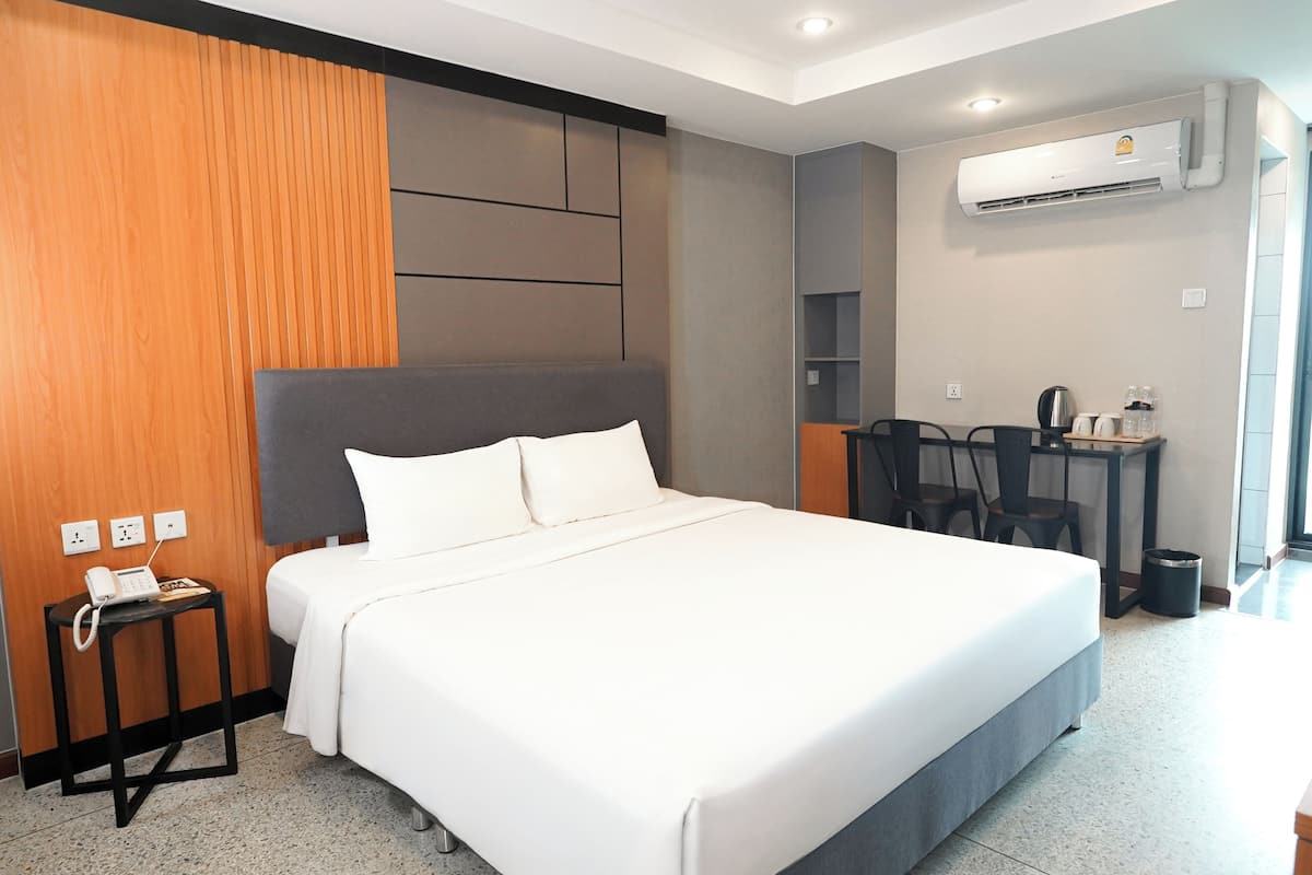 Une chambre d’hôtel avec un grand lit, un bureau avec des chaises, un appareil de climatisation et un téléphone sur une table de chevet.