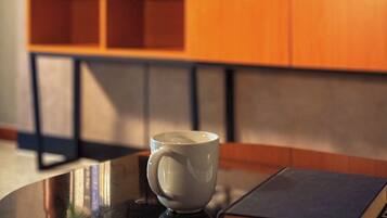 Una habitación con una mesa redonda, una taza blanca, un libro, un televisor y un armario de madera con libros y una planta.