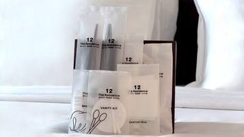 A hotel room with a neatly arranged vanity kit on the bed, including a sanitary bag and toiletries.