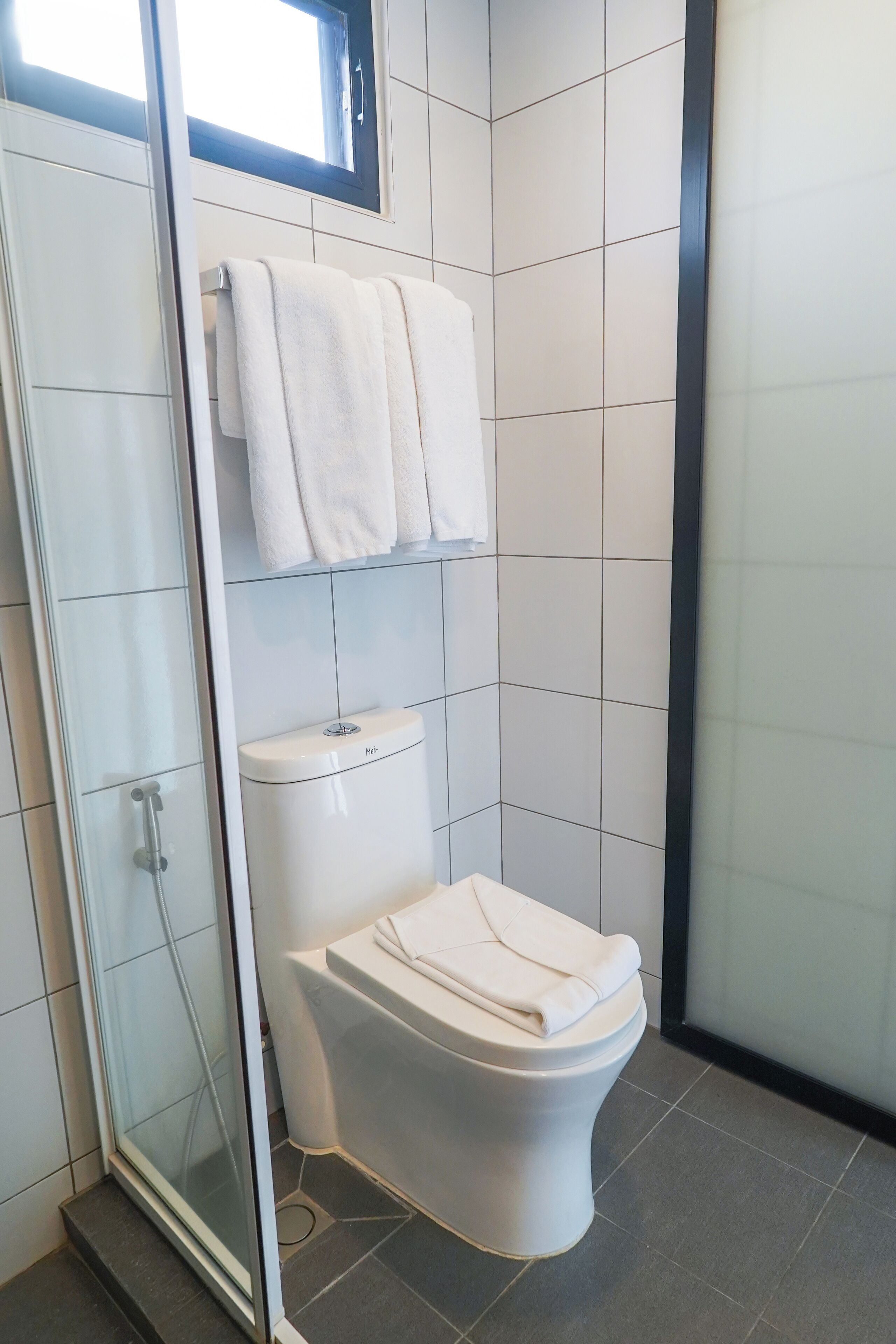 Een moderne badkamer met een douchecabine van glas, een toilet en een raam voor natuurlijk licht.