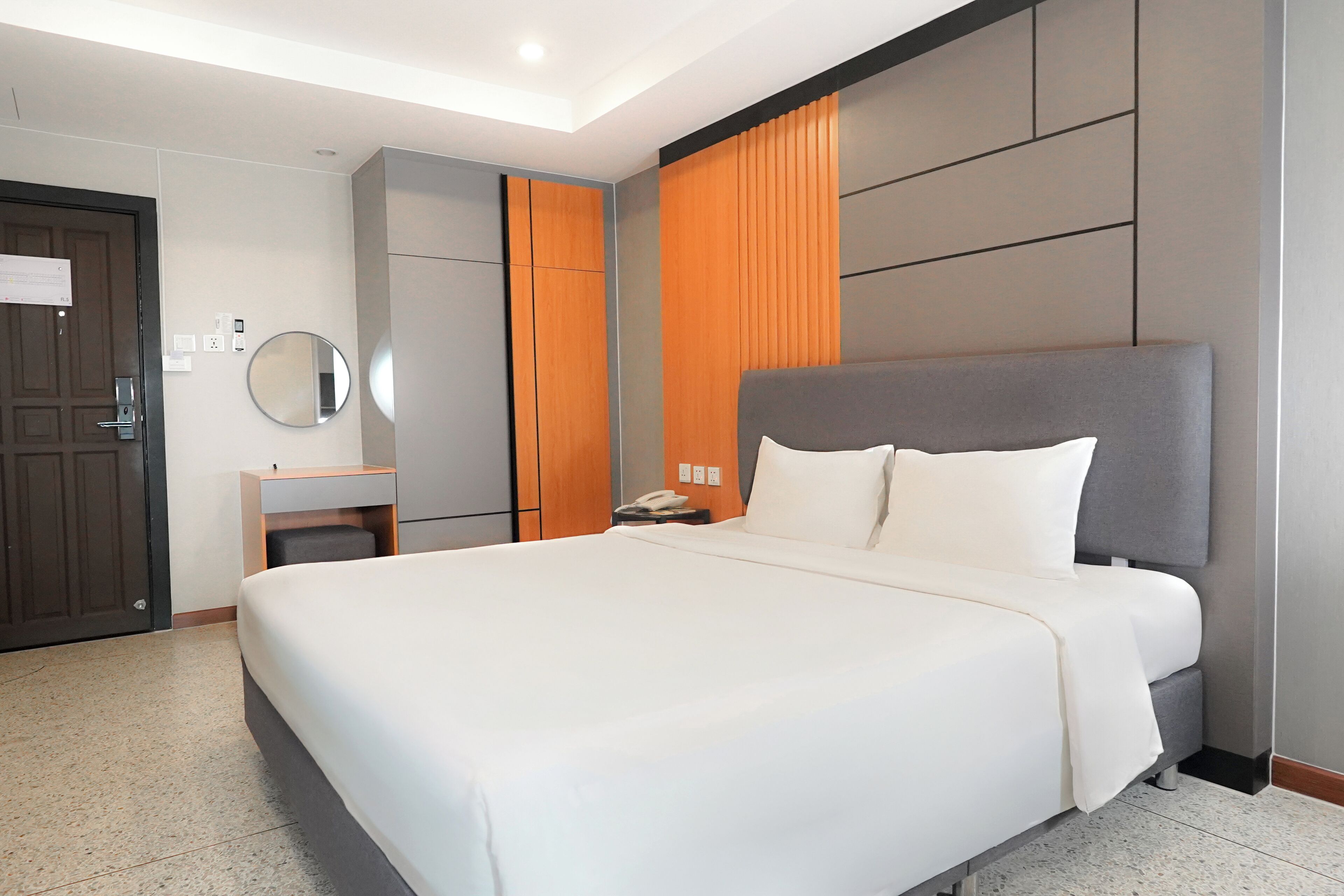 A hotel room with a large bed, a bedside table with a phone, a mirror, and a wardrobe.