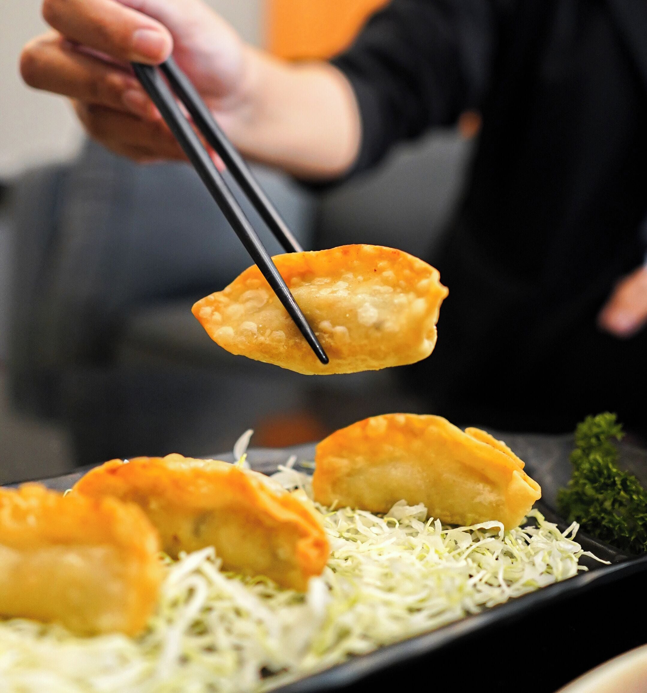 A person holding a fried food item with chopsticks over a plate with shredded vegetables.