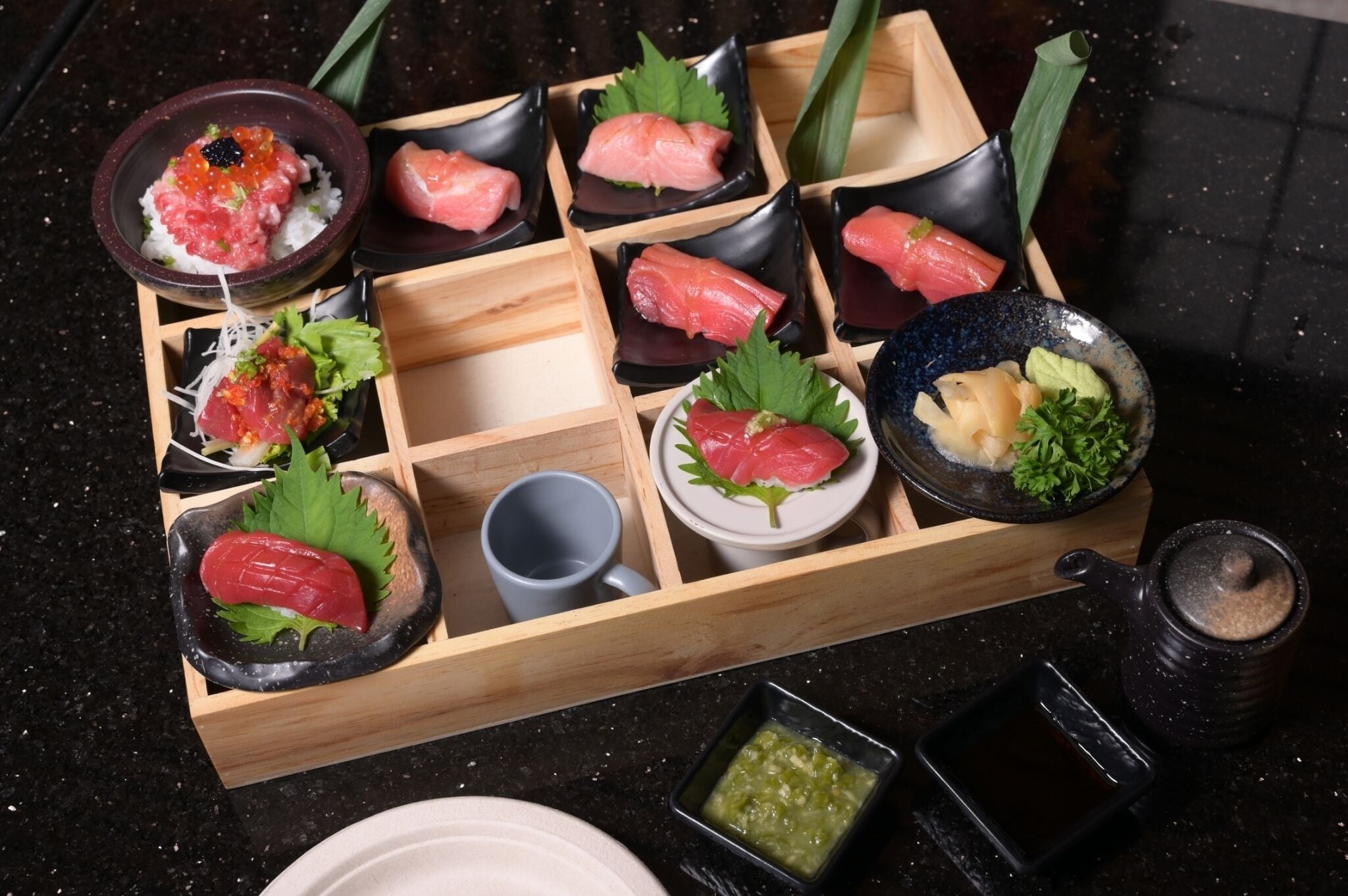 A wooden tray with various types of sushi, including sashimi and nigiri, accompanied by small bowls of soy sauce and wasabi.