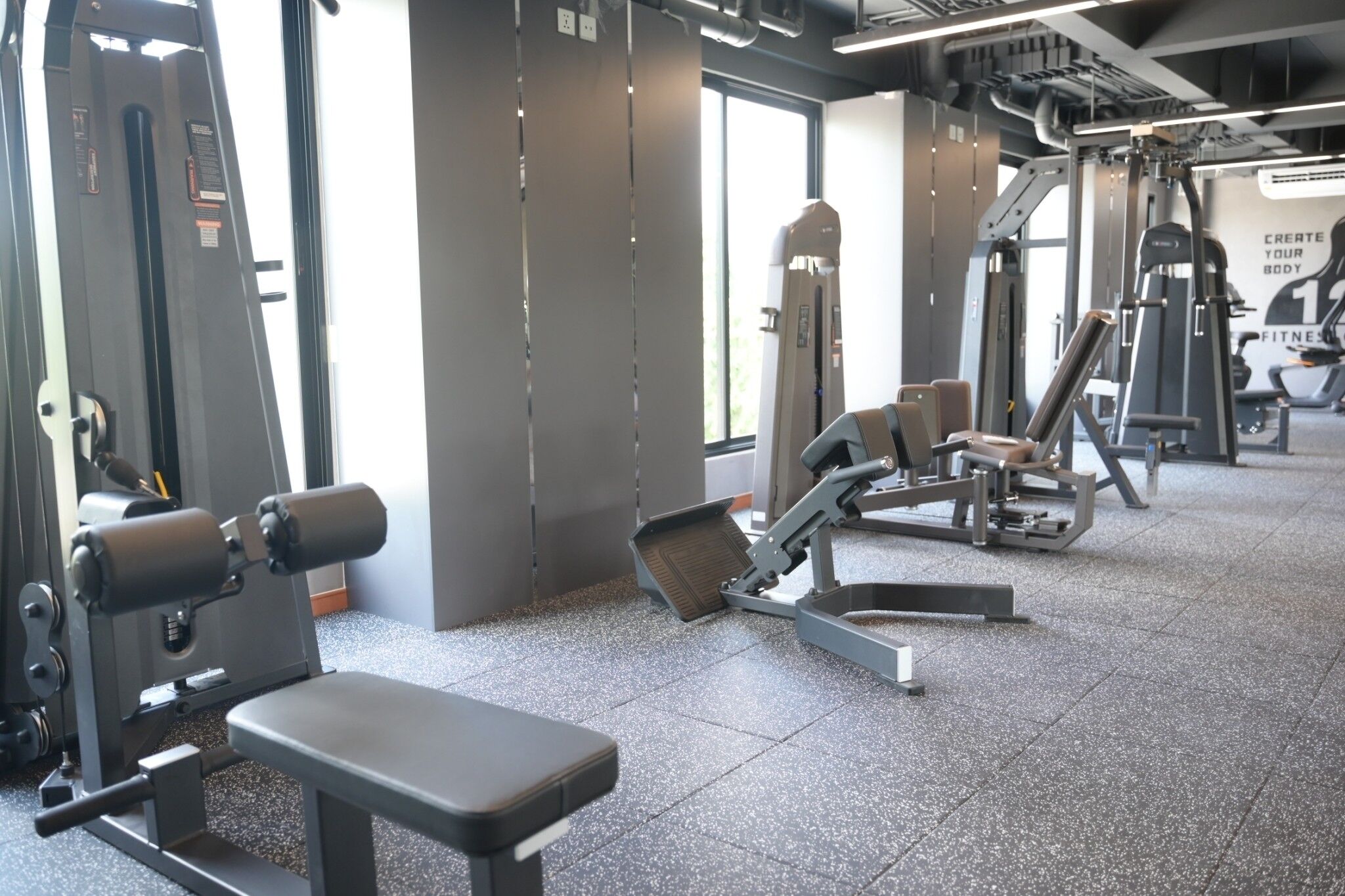 A gym with various exercise machines, a bench, and a large window providing natural light.