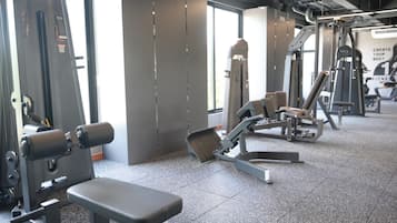 A gym with various exercise machines, a bench, and a large window providing natural light.