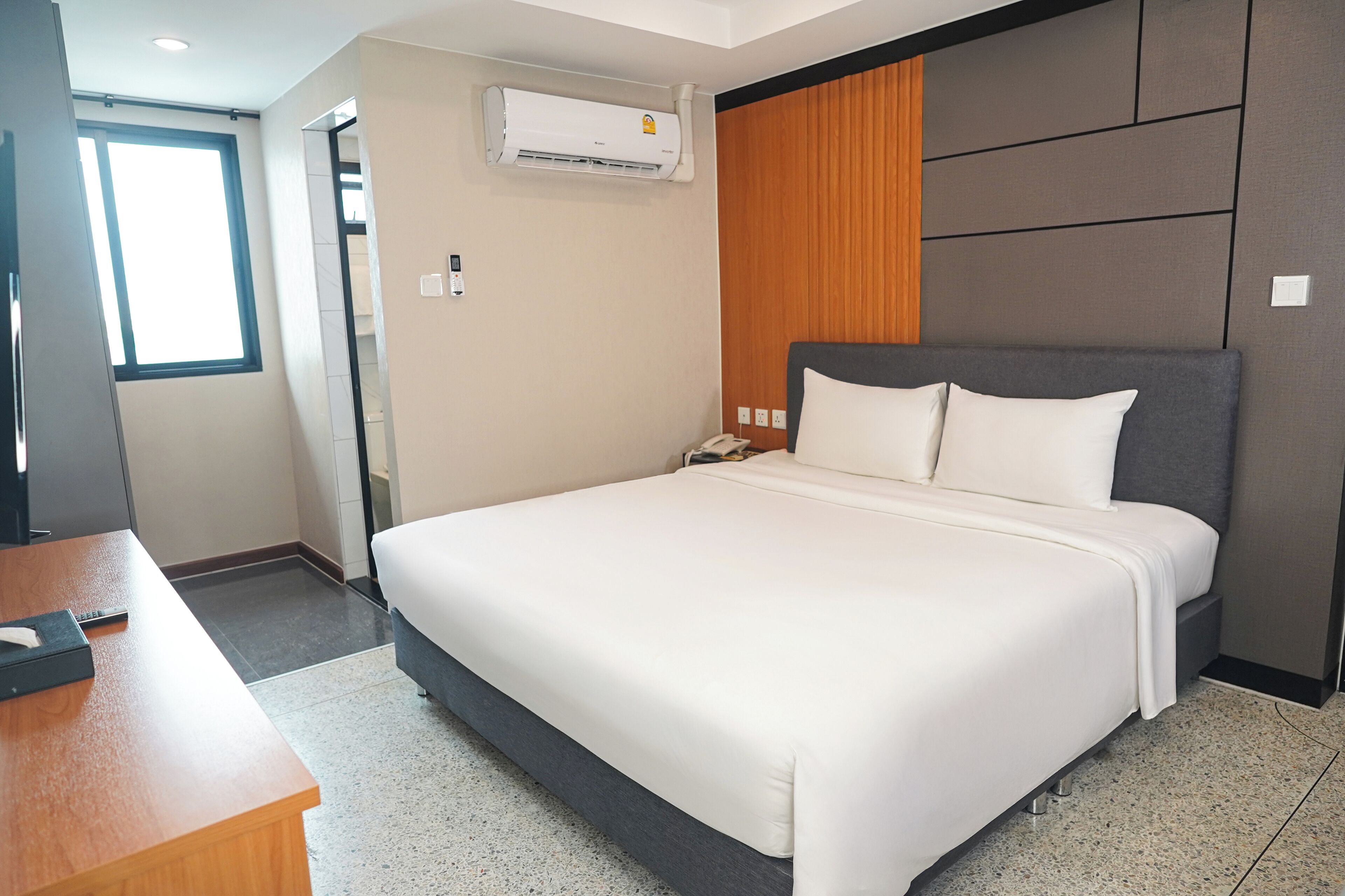 Habitación de hotel con una cama grande, cabecera de madera, un escritorio y un equipo de aire acondicionado en la pared.