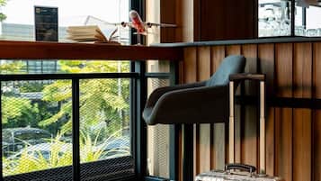 A modern hotel lobby with a wooden wall, a bar area, a suitcase, and a view of greenery outside.