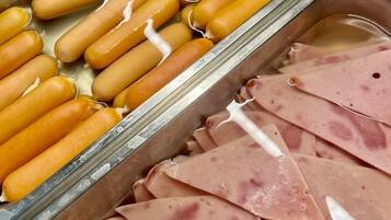 En buffet med hotdogs og skiveskåret skinke.
