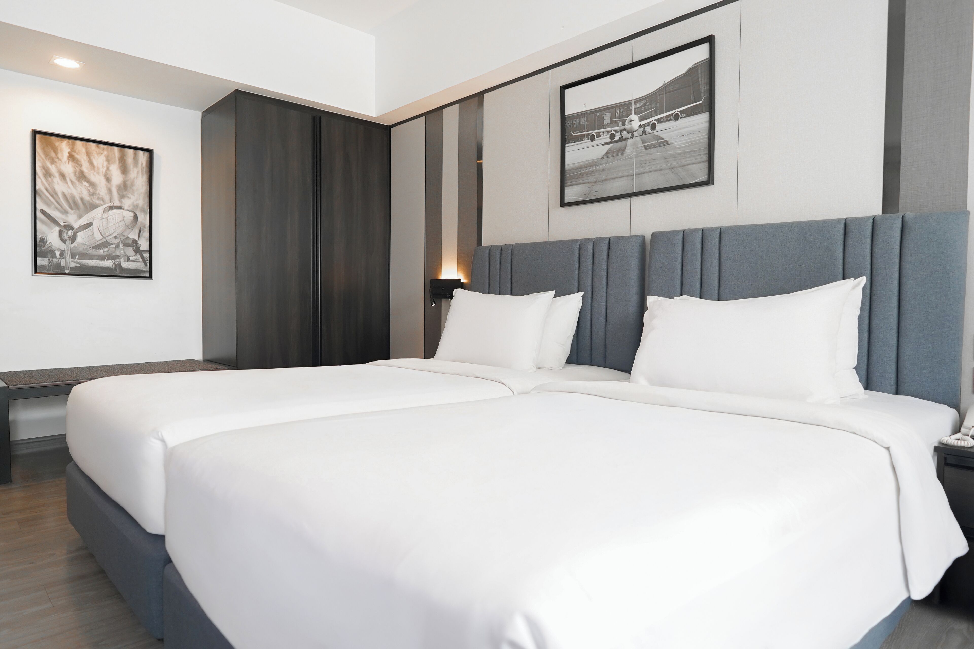 A modern hotel room with a large bed, a bedside table, a nightstand, and a wall-mounted lamp.