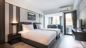 Une chambre d’hôtel avec deux lits, un bureau, une chaise, un appareil de climatisation et une fenêtre avec des rideaux.