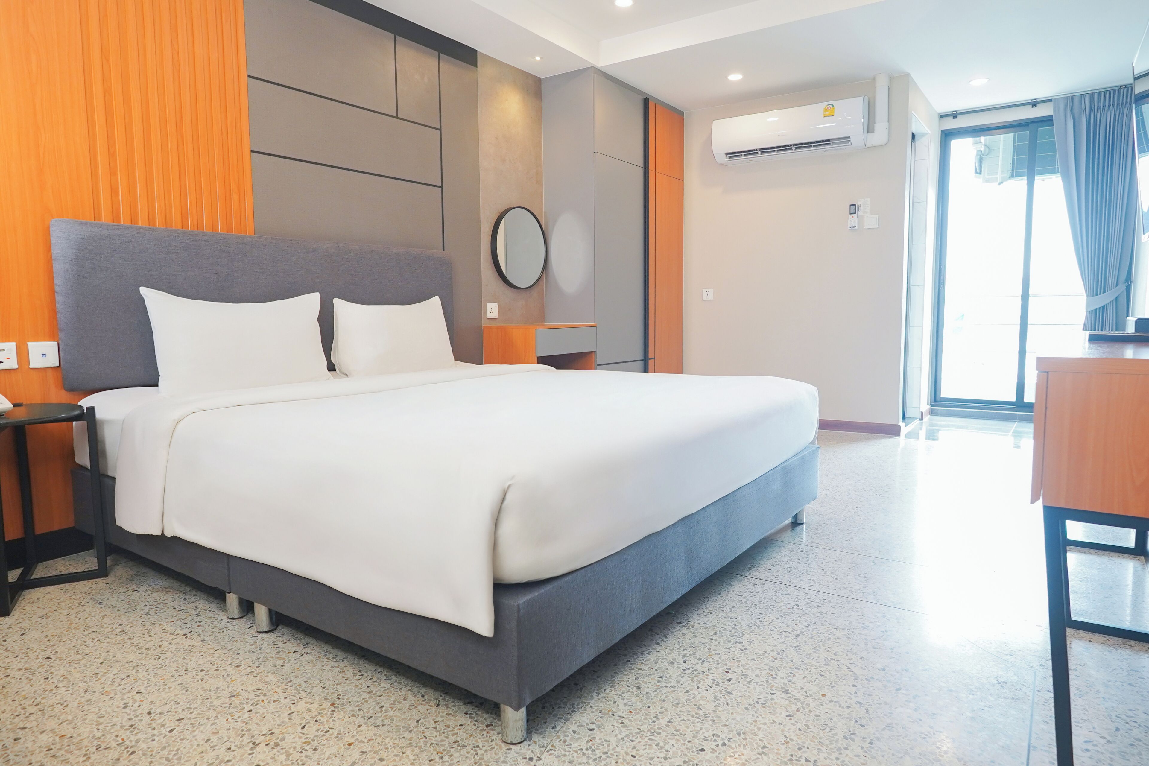 Una habitación de hotel moderna con una cama grande, una mesita de noche, un espejo y un equipo de aire acondicionado.