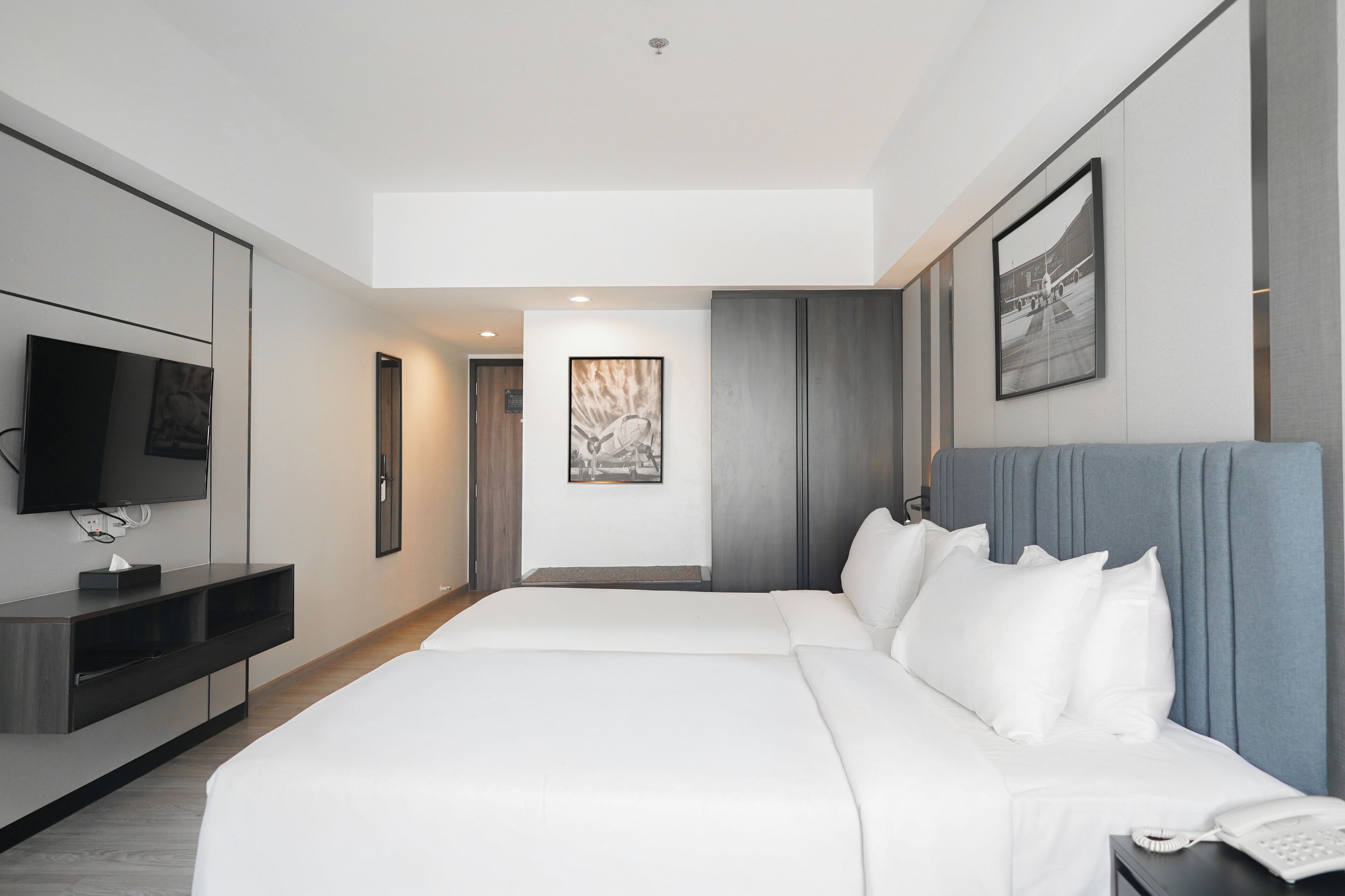 Una habitación de hotel moderna con una cama grande, un televisor de pantalla plana, una mesita de noche con un teléfono y una obra de arte enmarcada en la pared.