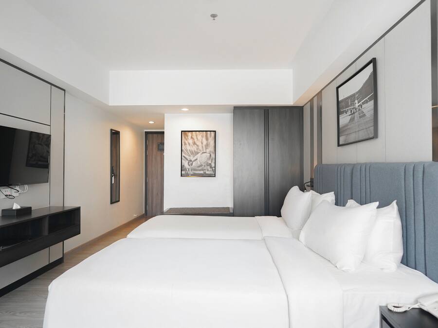 Una habitación de hotel moderna con una cama grande, un televisor de pantalla plana, una mesita de noche con un teléfono y una obra de arte enmarcada en la pared.