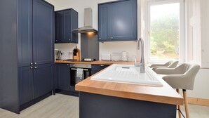 A modern kitchen with dark blue cabinets, a wooden countertop, a built-in sink, and a window providing a view of greenery outside.