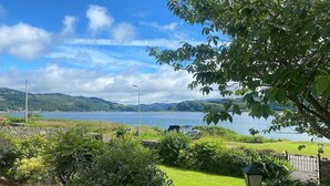 A view of a lake with hills in the background, a paved path, and a bench.