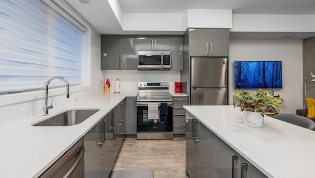 A modern kitchen with stainless steel appliances, a large island, and a flat-screen TV mounted on the wall. - Elegant Apartment,  5mins from the Falls (Niagara Falls)
