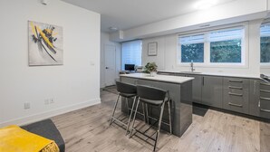 A modern kitchen with a central island, bar stools, and a large window providing natural light. - Elegant Apartment,  5mins from the Falls (Niagara Falls)