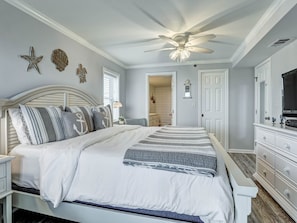 Une chambre à coucher comprenant un lit, des tables de chevet, une commode, un ventilateur de plafond et des œuvres d’art décoratives murales.