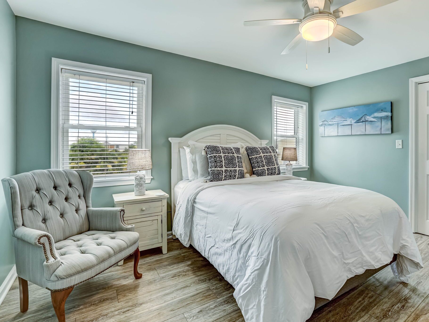 A bedroom with a white bed, a tufted armchair, and a ceiling fan.