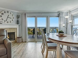 A dining area with a wooden table, chairs, and a view of the sea through large glass doors.