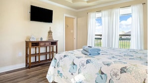 Ein Schlafzimmer mit einem großen Bett, einem Deckenventilator, einem an der Wand befestigten Fernseher und Blick ins Freie.