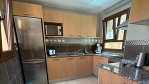 A modern kitchen with wooden cabinets, a stainless steel refrigerator, a microwave, and a sink. There are two trash bins and a window providing natural light. - Sunset Beach 4 Floor Villa 200m to Beach+Fast WIFI (Corralejo)