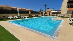 A rectangular swimming pool with clear blue water, surrounded by white lounge chairs and a grassy area. - Sunset Beach 4 Floor Villa 200m to Beach+Fast WIFI (Corralejo)
