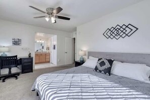 Quarto com cama, escrivaninha, cadeira, ventoinha no teto e um objeto decorativo na parede.