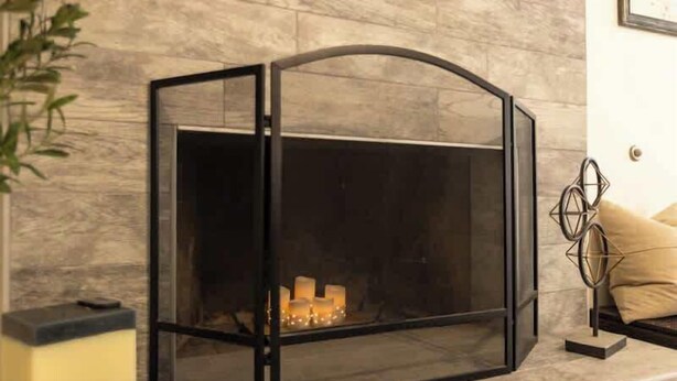 Una chimenea moderna con recinto de vidrio, pared de mármol y una escultura de metal decorativa.
