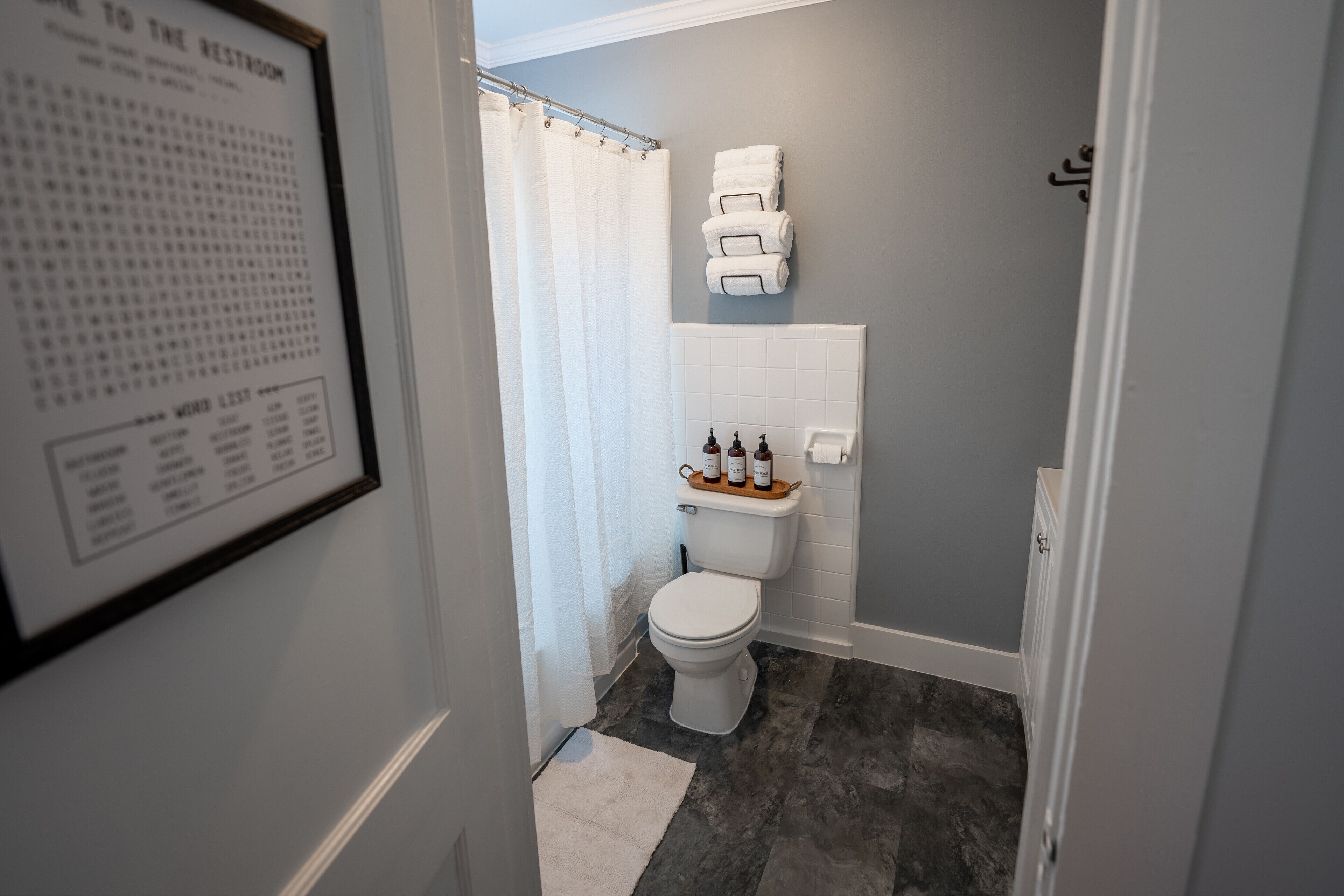 Une salle de bain avec des toilettes, un rideau de douche, une pile de serviettes et un panneau encadré accroché au mur.