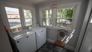 A laundry room with a washing machine, dryer, and a wicker chair by the windows. - Comfy vintage cottage in beautiful small town--7mins from everything. (Newton)