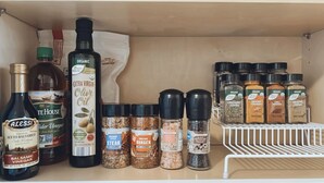 A kitchen shelf with various condiments and seasonings, including bottles of vinegar, olive oil, and spice jars. - Comfy vintage cottage in beautiful small town--7mins from everything. (Newton)