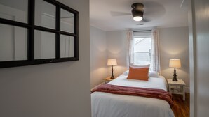 A bedroom with a bed, two bedside tables with lamps, a window with curtains, and a ceiling light fixture. - Comfy vintage cottage in beautiful small town--7mins from everything. (Newton)