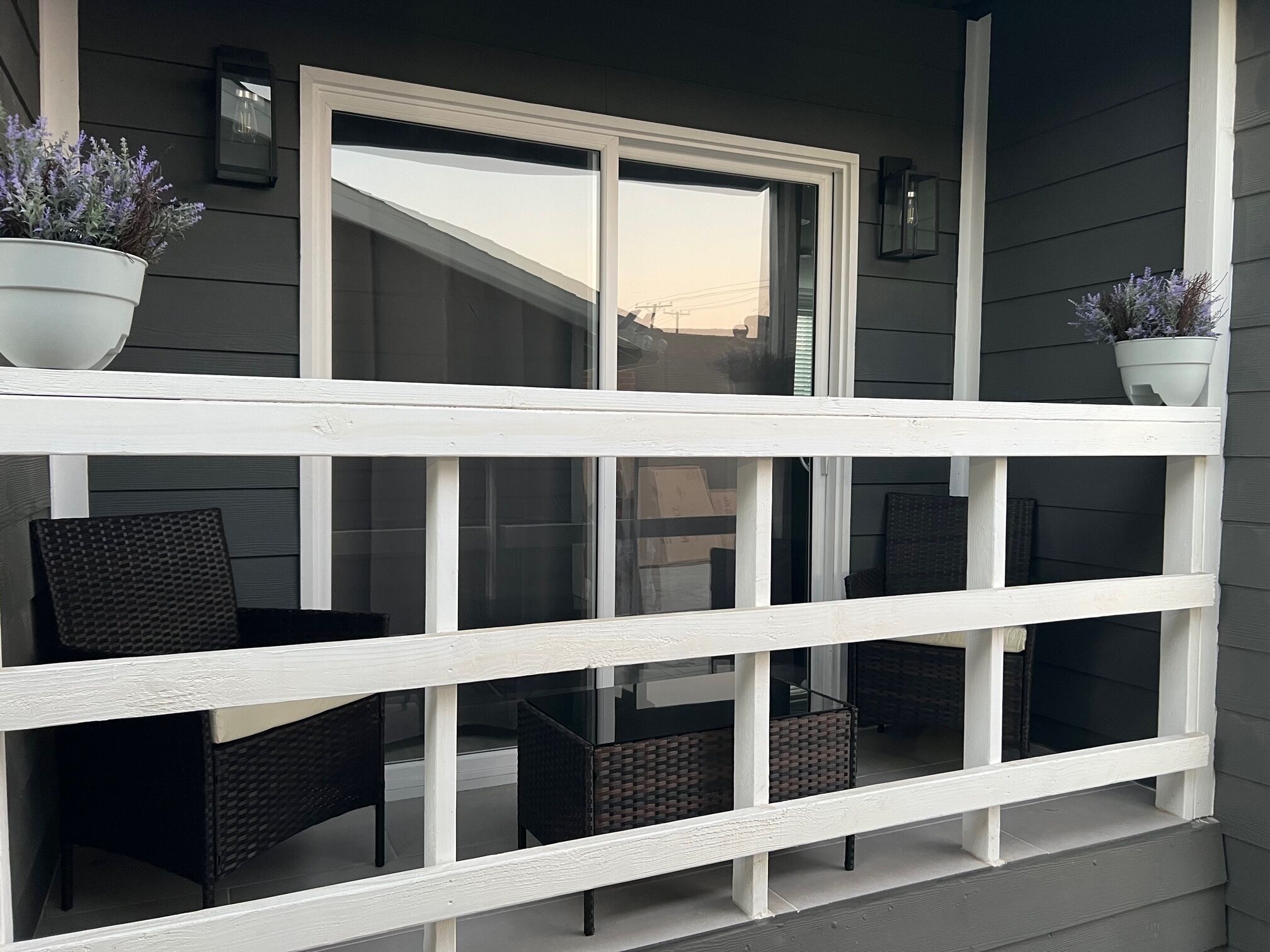 Un balcone con ringhiere bianche, due poltrone in vimini e due piante in vaso.