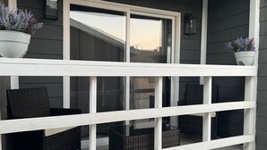 Ein Balkon mit weißen Geländern, zwei Korbstühlen und zwei Blumentöpfen.