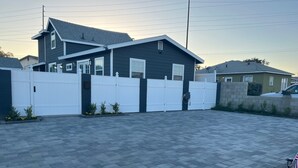 Ein Wohngrundstück mit einem befahrbaren Einfahrtstor, ein Haus mit dunkler Fassade und einem gepflasterten Weg.