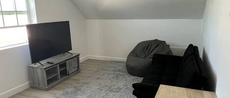 A modern living room with a flat-screen TV on a wooden stand, a grey shag rug, a black bean bag chair, and a small wooden table.