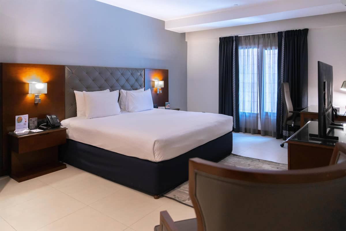 Une chambre d’hôtel avec un grand lit, deux tables de chevet avec des lampes, une télévision et un fauteuil.