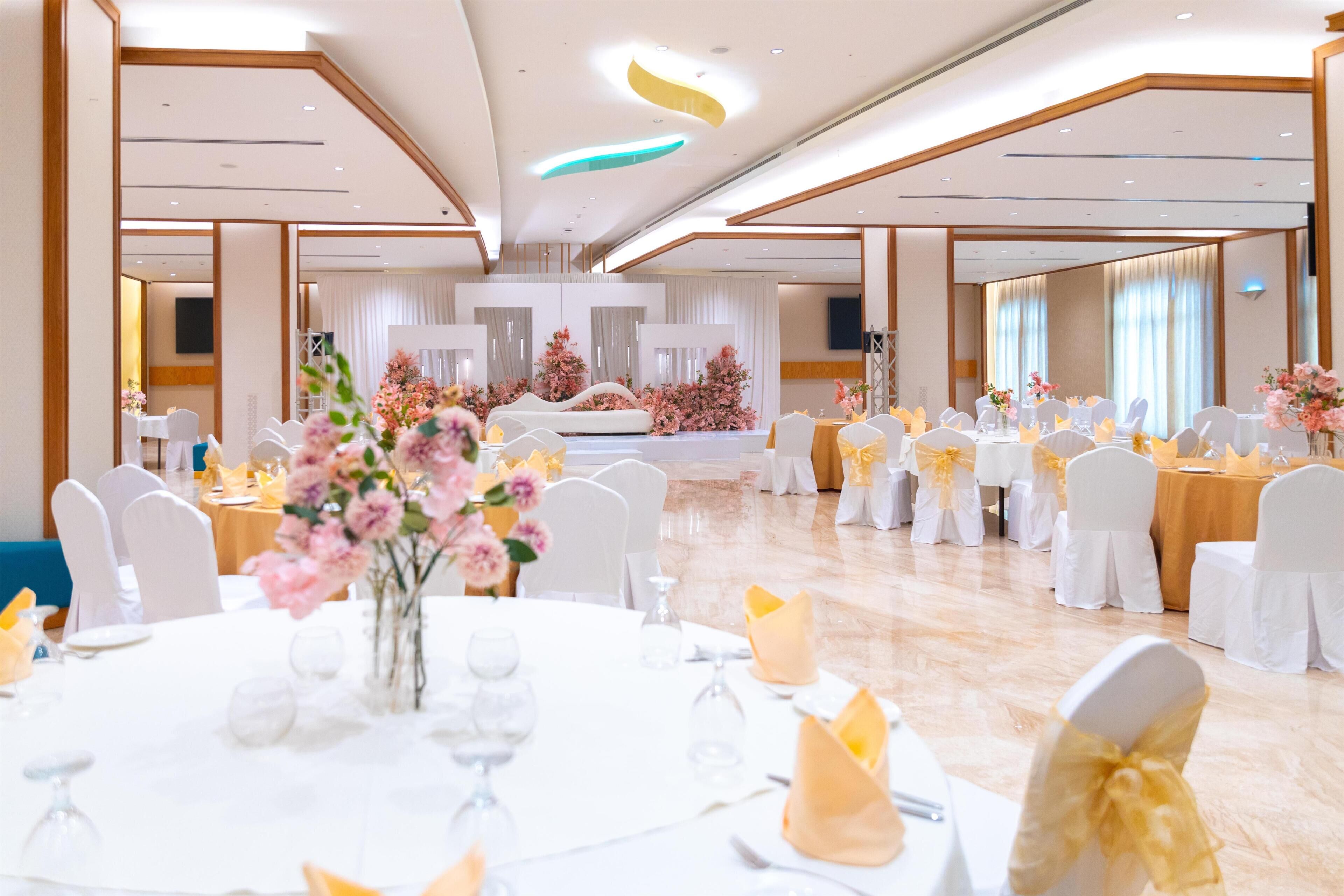 A spacious banquet hall with round tables, white chairs, and floral centerpieces.