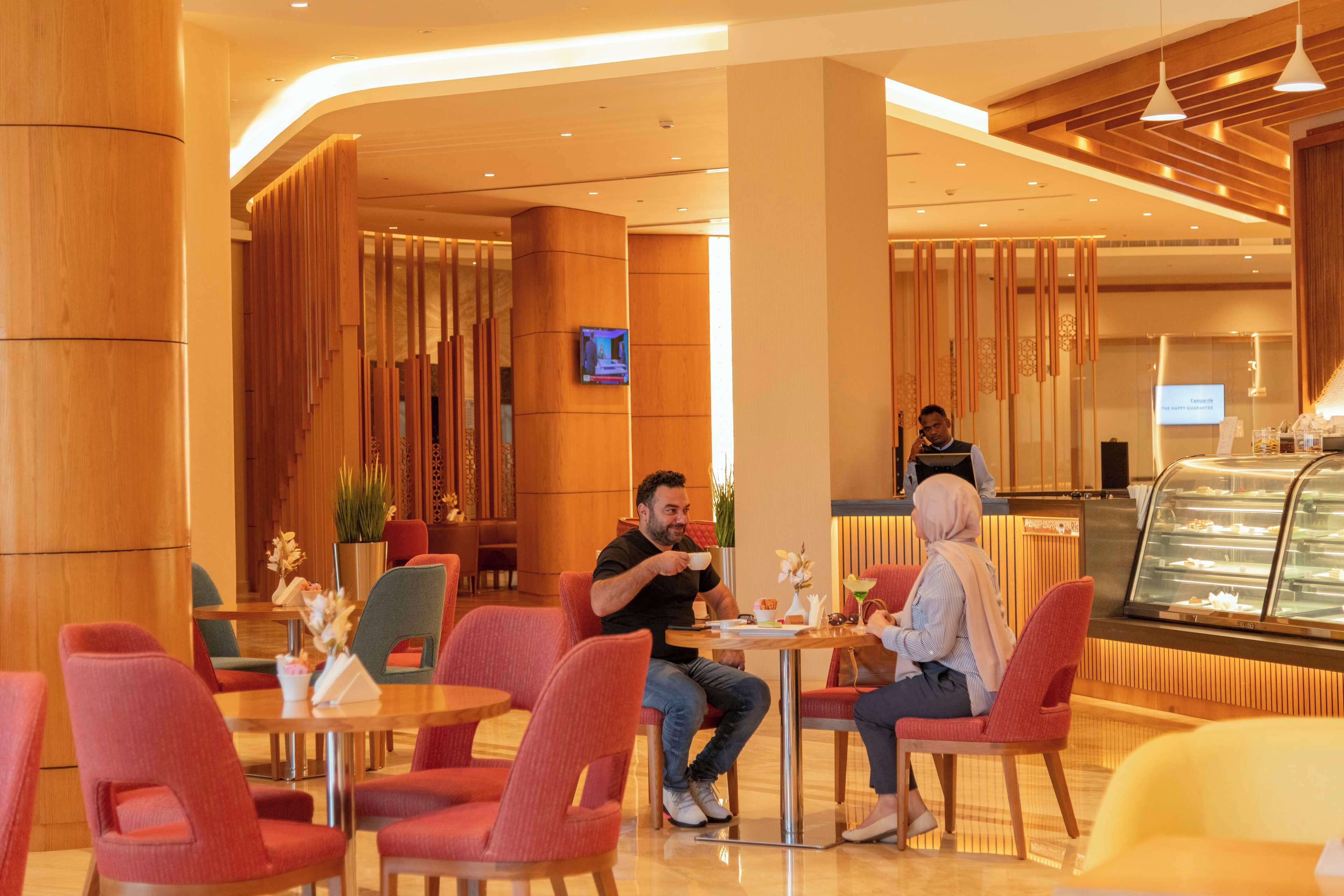 Un moderno vestíbulo de hotel con sillas rojas, una recepción y una mesa con postres.