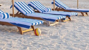 Strandstoelen met gestreepte handdoeken, een volleybal en parasols.