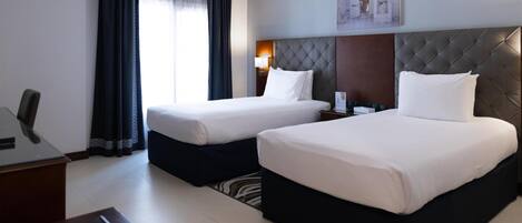 A hotel room with two beds, a desk, a chair, a lamp, and a painting on the wall.