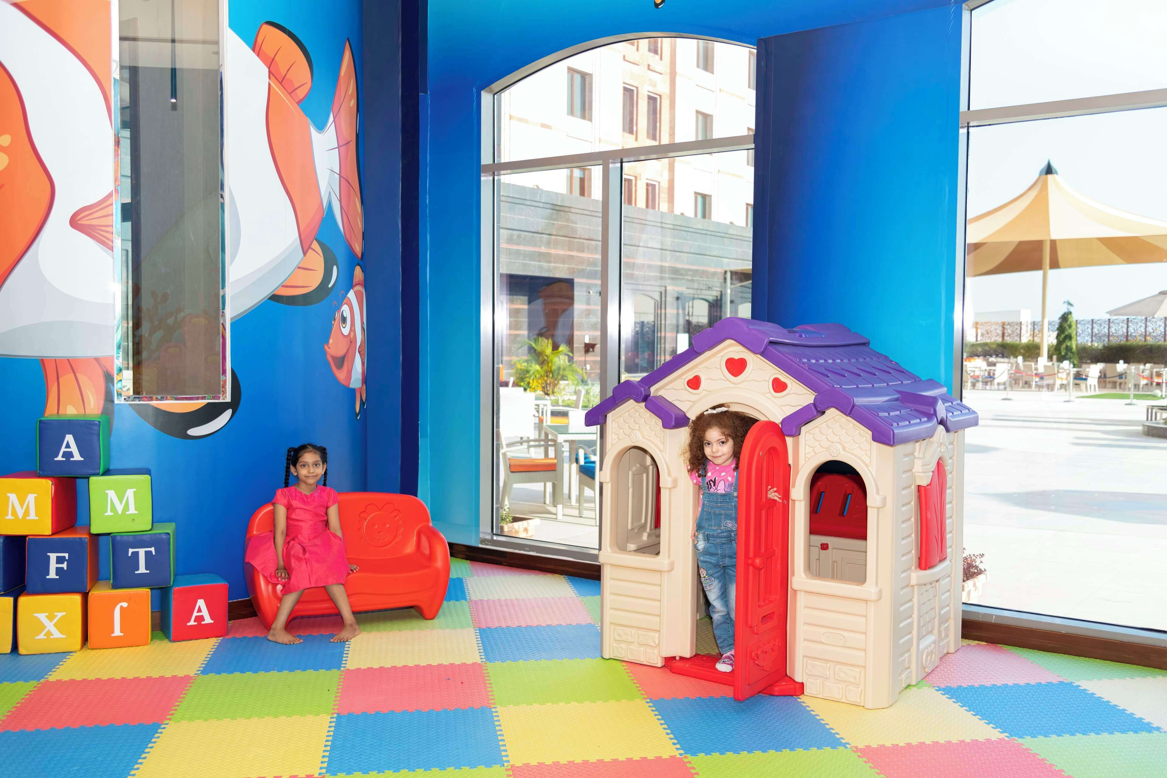 A play area with colorful blocks, a playhouse, and a large window with a view of the outside.