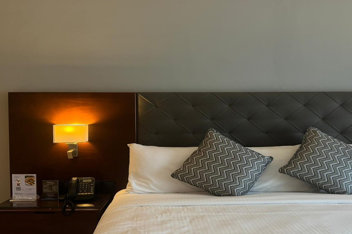 Habitació d'hotel amb un llit, dos almoinos, una tauleta de nit amb una làmpada, un telèfon i un cartell de menú.