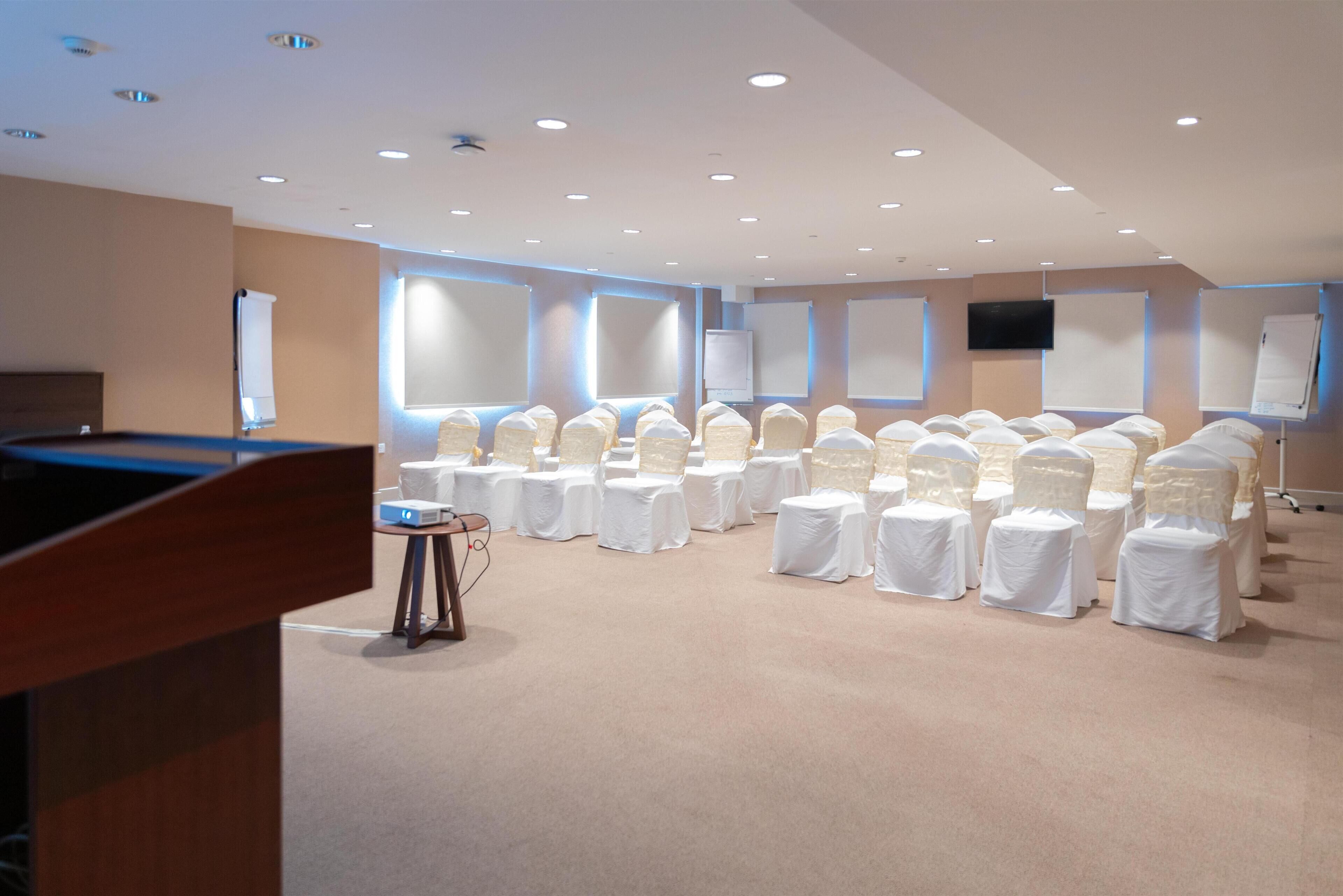 A conference room with rows of chairs, a podium, and presentation screens.