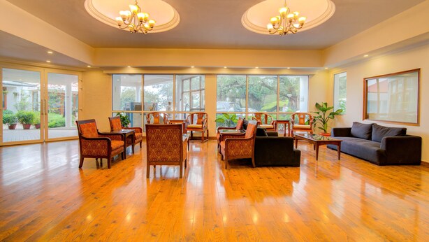 A spacious room with wooden flooring, multiple seating areas, and large windows offering natural light and views. - Timber Trail Resort (Kasauli)