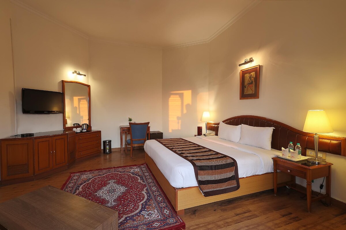 Una habitación de hotel con cama, mesitas de noche, televisor, escritorio y silla.